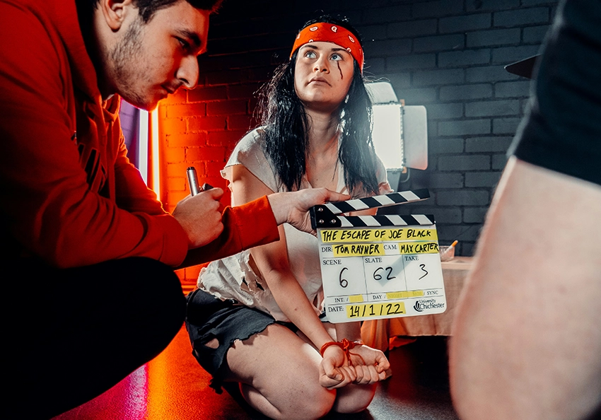 A group of film students slate a scene in a dark room.
