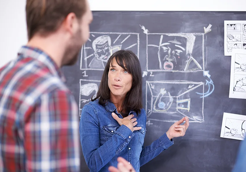 a woman explaining storyboards drawn on a chalkboard