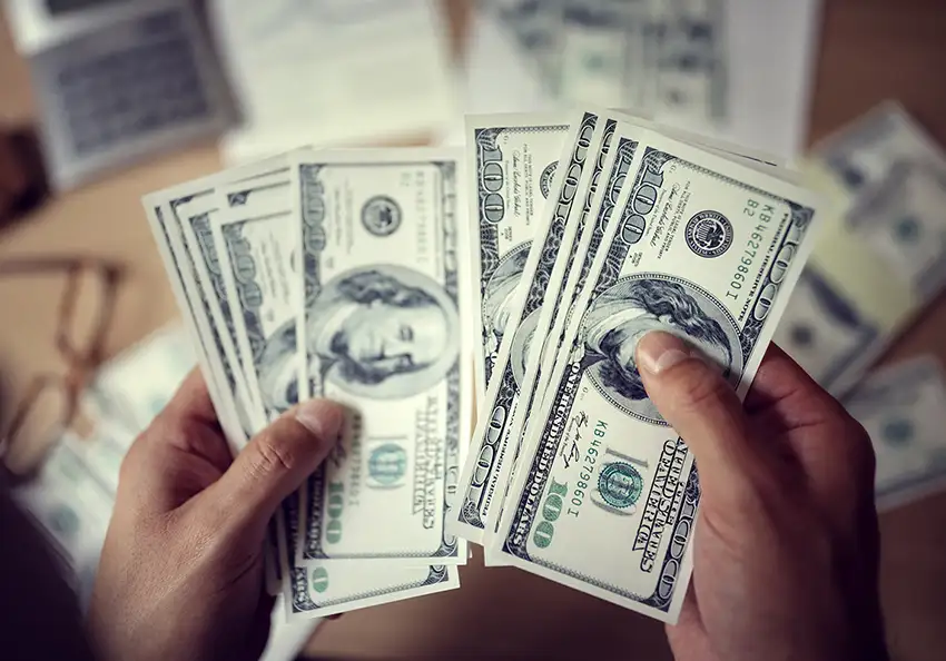 Hands holding $100 dollar bills.